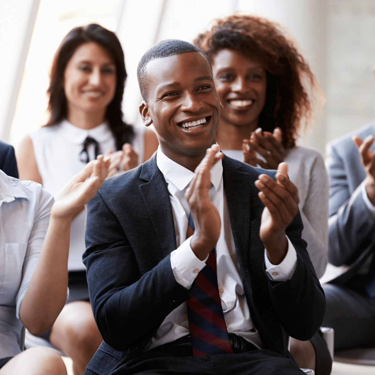 A group of business men and women wearing formal attire, smiling and clapping whilst sitting down. This symbolises how ap invoice automation can improve trading partner relationships.