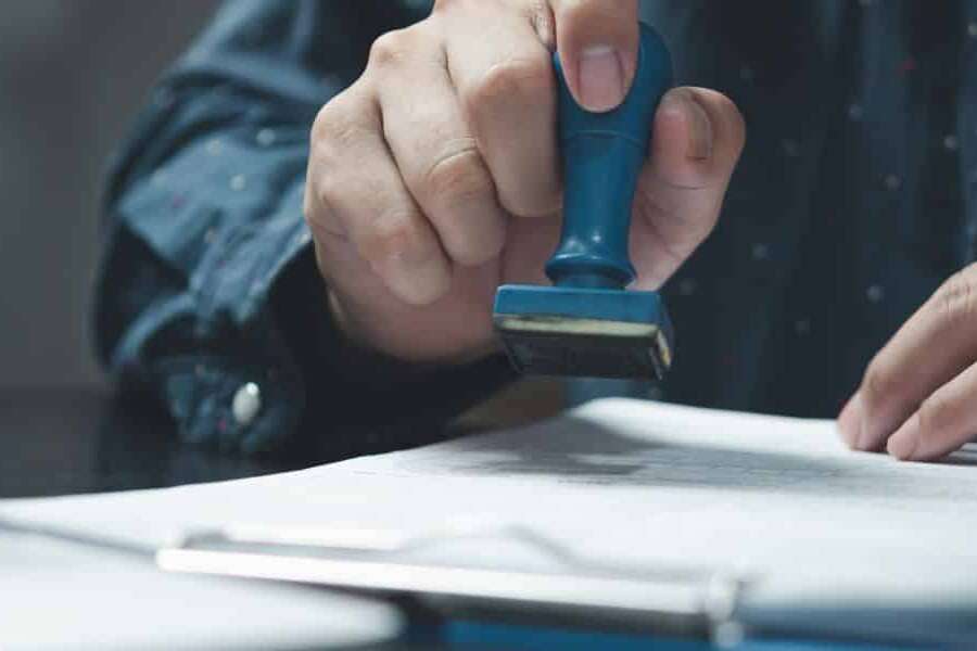 Close up photo of a governmental executive holding an approval stamp ready to sign-off an official document. Representing a blog focused on how businesses can remain on top of tax regulatory compliance