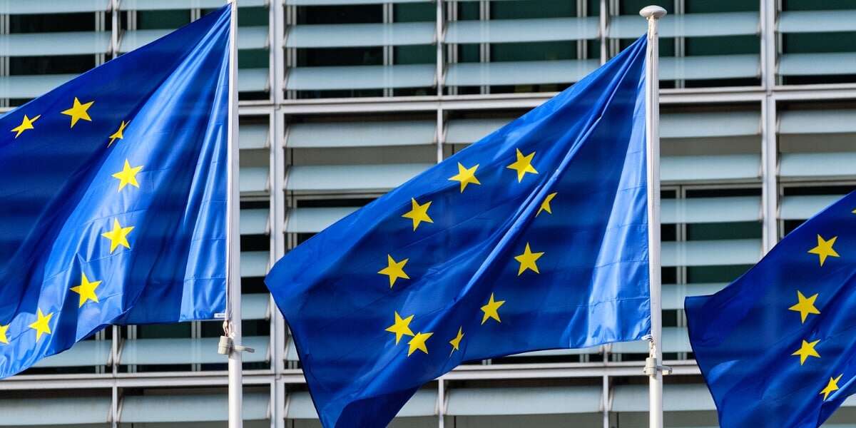 Photo of 3 EU flags flying outside a governmental building. Representing a blog titled 'ViDA: Everything you should know about VAT in the Digital Age'