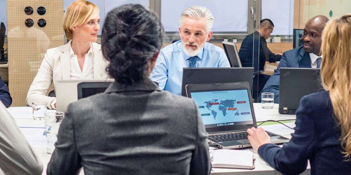 Photo of a corporate board team having a meeting in a board room with laptops. Representing a blog titled 