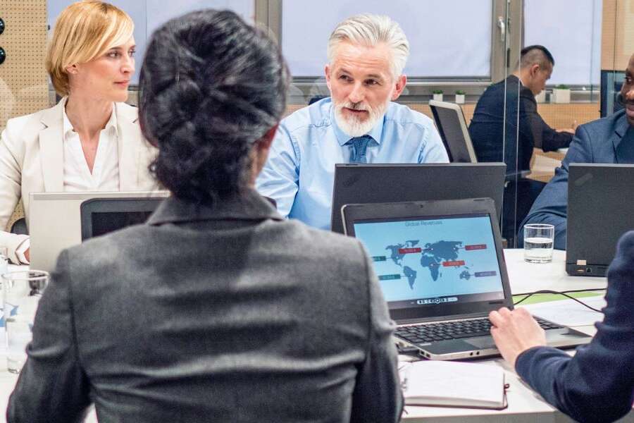 Photo of a corporate board team having a meeting in a board room with laptops. Representing a blog titled 